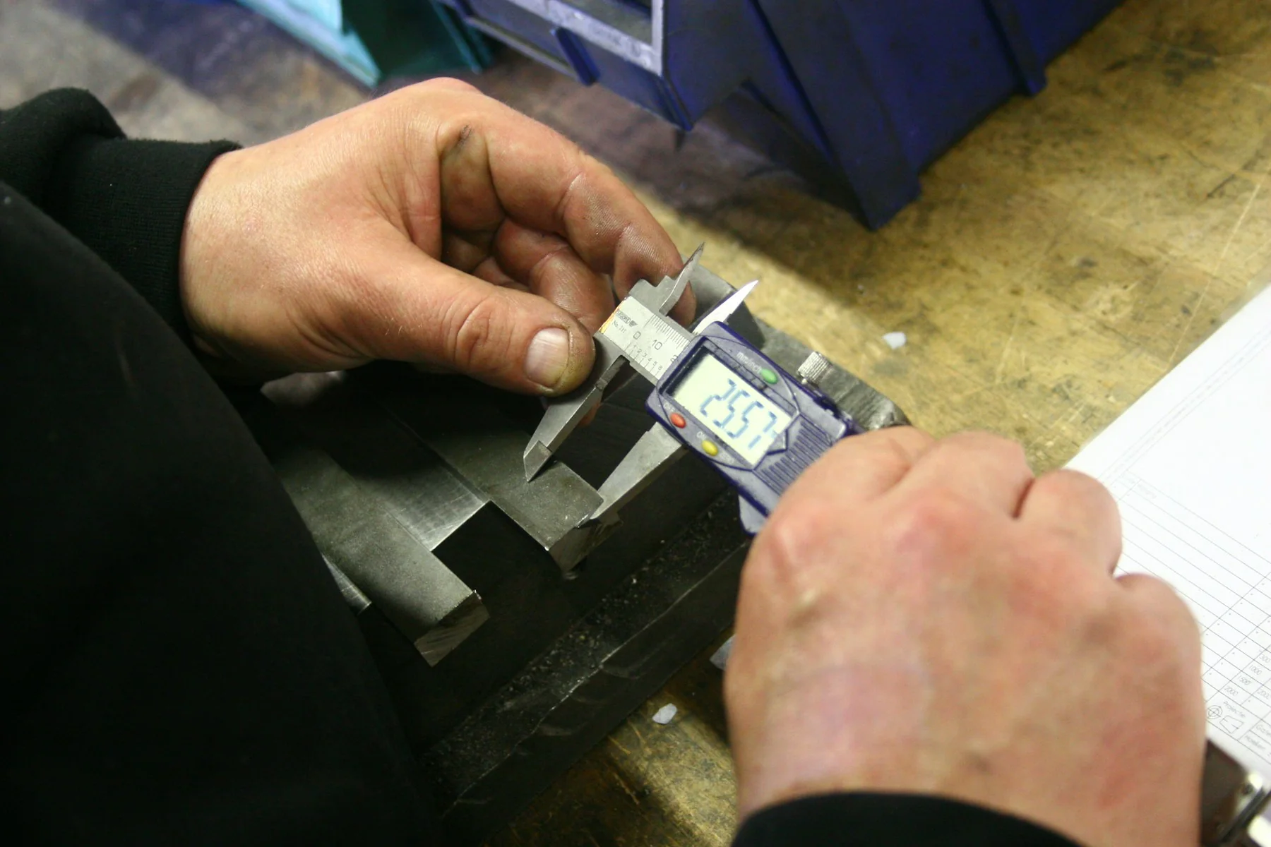 Hands measuring a component with digital calipers; representative inspection photograph