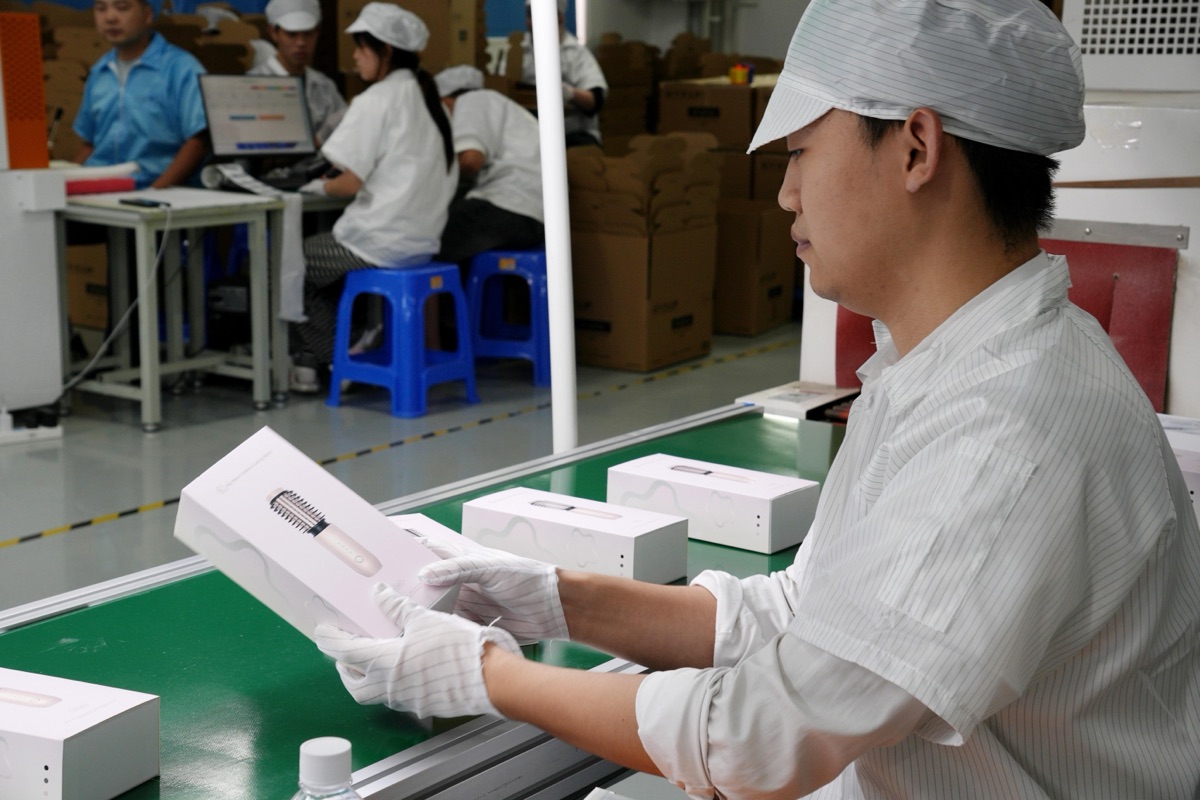 Operator inspecting packaged hair care devices on the production line